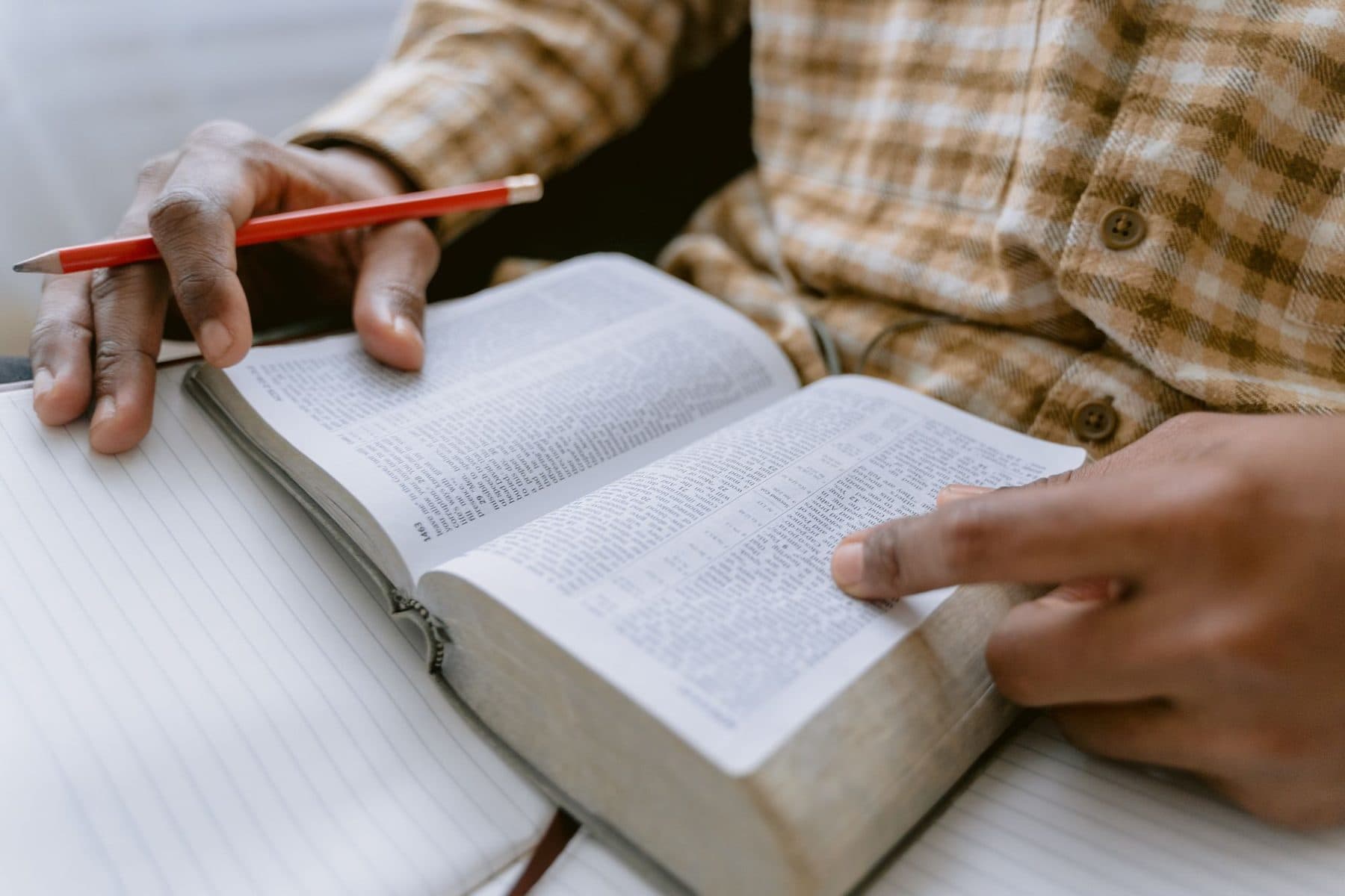 Hands holding an open Bible, making notes in the margin with a pencil