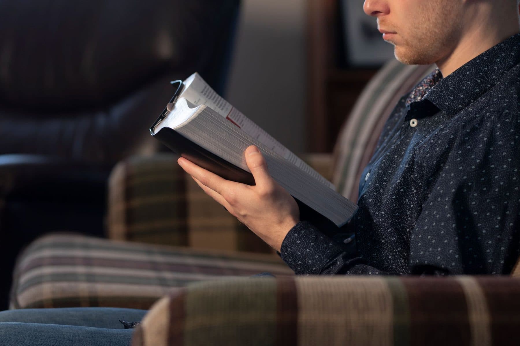 A man sitting in a chair reading a Bible